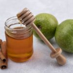 front view honey in a jar with a wooden spoon cinnamon and green apples on a white background
