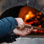 man puts pizza in a professional brick oven with red light due to the fire inside the oven