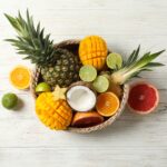 Wicker basket with exotic fruits on white wooden background, top view and space for text